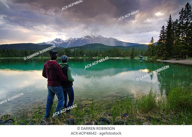 Couple enjoy the view of Lake Edith and Mount Pyramid in the Rocky Mountains, near Jasper, Alberta, Canada