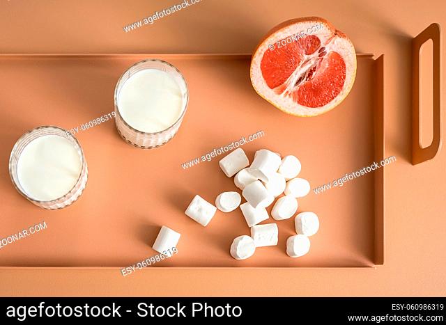 Tasty grapefruit on the orange metal support on the same table in the studio. Next to it there are two glasses with milk and pile of marshmallows