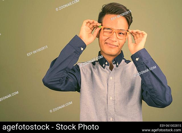 Studio shot of young teenage Indian man looking smart against colored background