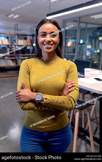 Portrait of smiling multiracial businesswoman standing with arms crossed at modern workplace