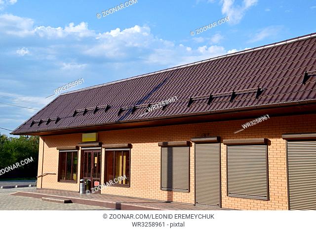 The roof of corrugated sheet on a building. Brown roofing metal sheets on Rented store. Brown shutters on the windows