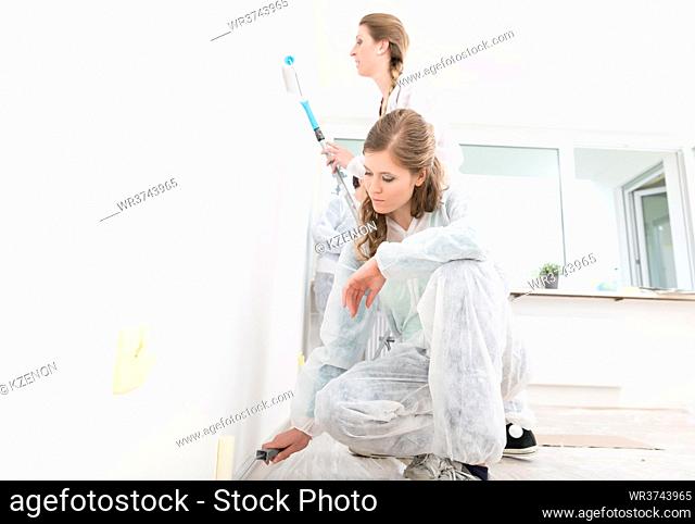 Close-up of two female worker painting the wall with roller at home
