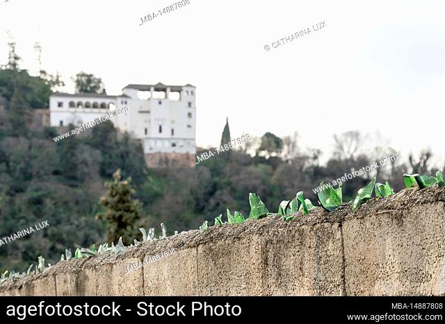 Spain, Andalusia, Granada, wall with broken glass, in the distance the Palacio de Generalife (blurred), symbolic image