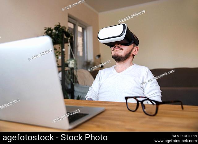 Man wearing virtual reality simulator in front of laptop at home