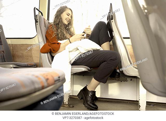 young woman sitting in public transport, using phone, in city Cottbus, Brandenburg, Germany