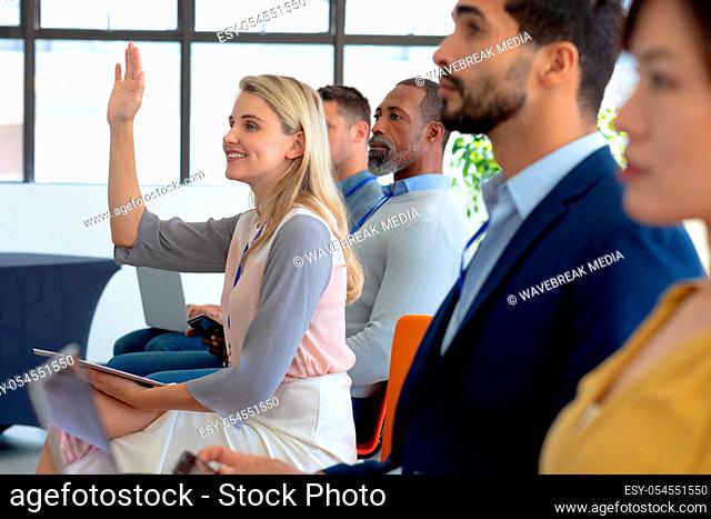 Side view of a diverse group of business creatives sitting in a row in the audience at a business conference, with one blonde haired Caucasian young woman...
