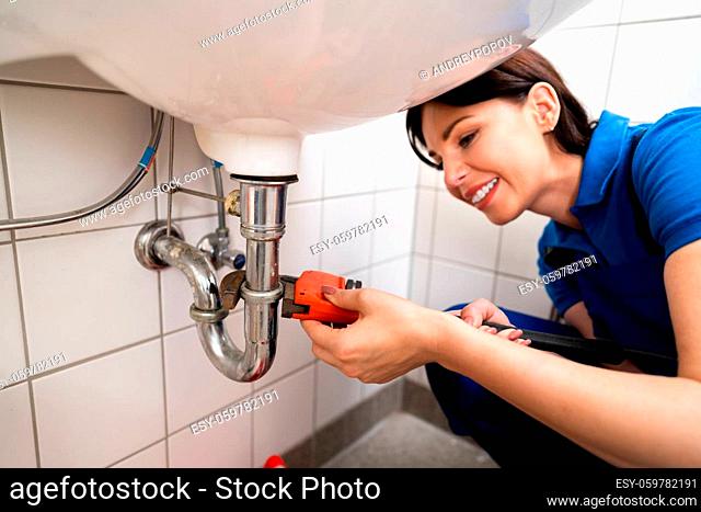 Young Plumber Fixing A Sink In Bathroom
