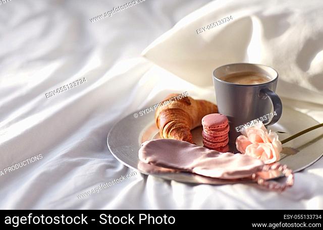 croissant, coffee and eye sleeping mask in bed