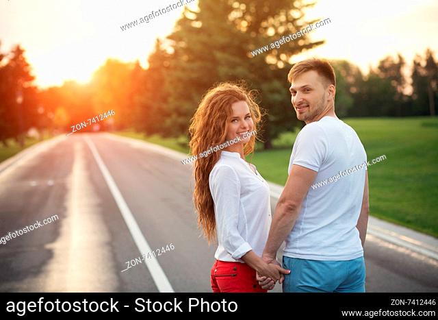 Happy couple holding hands in the sunset. Man and woman in white T-shirts smiling