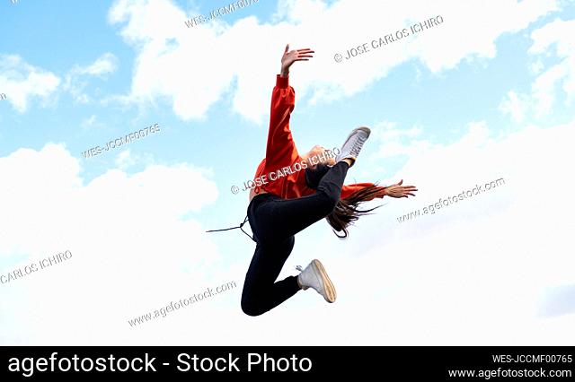 Long-haired brunette jumping against sky