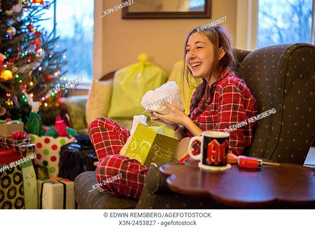 Young woman opening Christmas present wearing plaid pajamas in Fallston, Maryland, USA