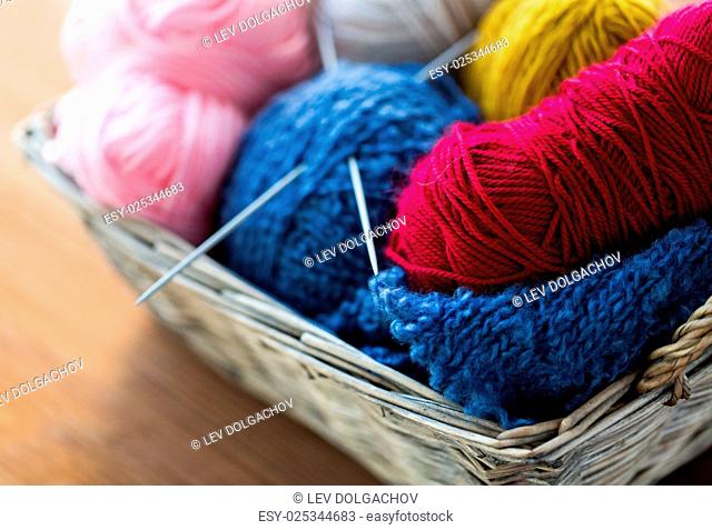 handicraft and needlework concept - close up of wicker basket with knitting needles and balls of yarn