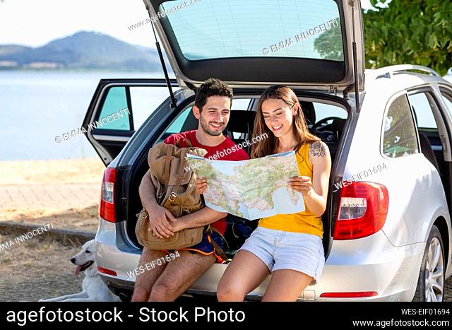 Smiling couple checking map while sitting in car trunk