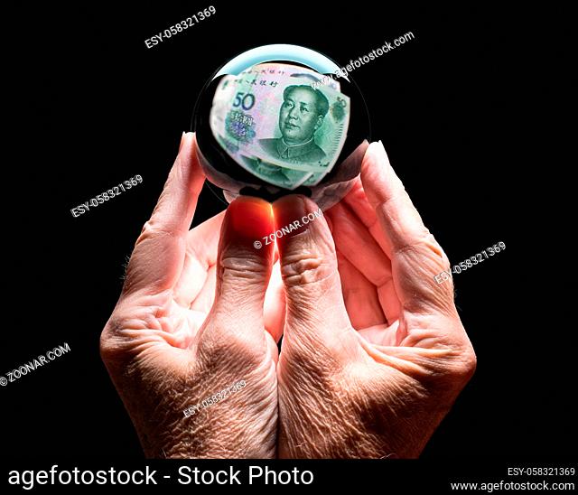 Senior caucasian hands holding a crystal futures or fortune ball reflecting a China 50 Yuan note as concept for the exchange rate for the currency