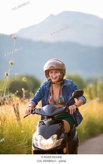 Happy young woman riding moped on rural road, Majorca, Spain