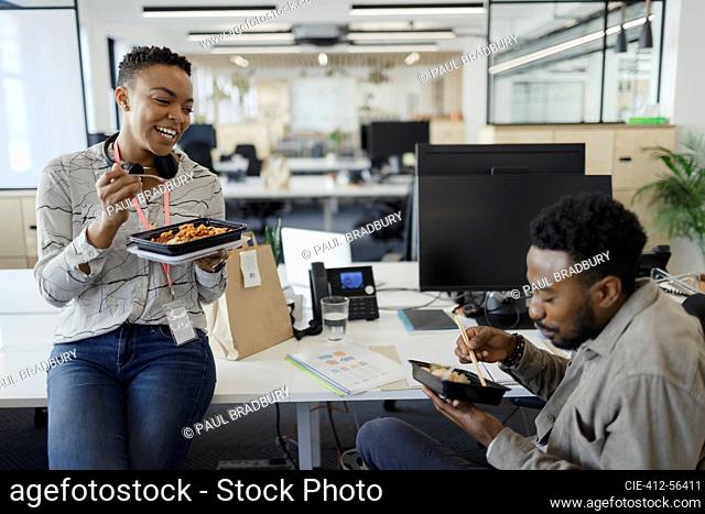 Gente de negocios feliz comiendo comida para llevar en el escritorio en la oficina de planta abierta