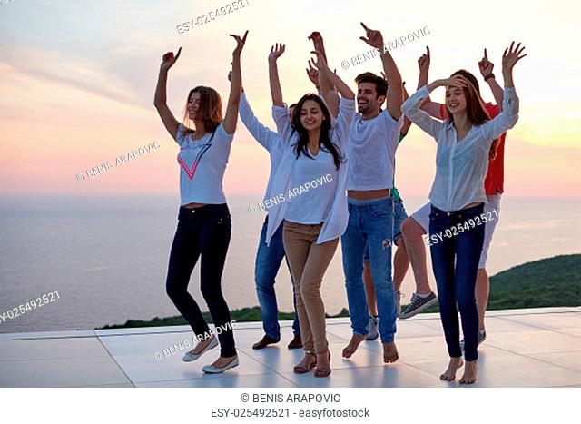 group of happy young people dancing and have fun on party in modern home bacony with sunset and ocean in background
