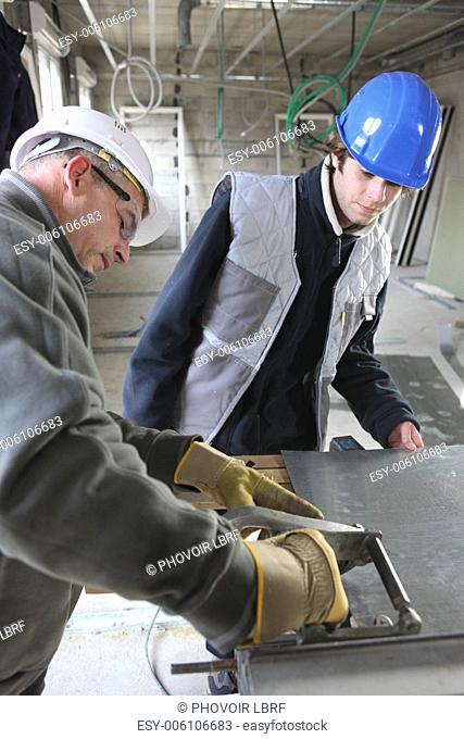 Two manual workers cutting sheet metal