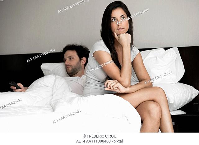 Woman sitting in bed while husband watching tv