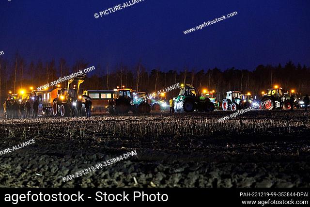 19 December 2023, Lower Saxony, Haselünne: Farmers from Lower Saxony stand in a field with illuminated agricultural machinery