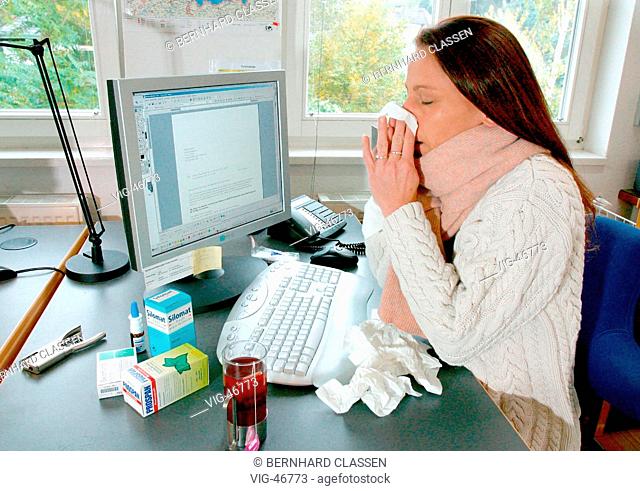 Feature: working in spite of illness ( Influenza ). Woman with a thick scarf, hankie and medicine on the office desk ( posed )