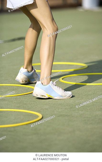 Teenage girl in tennis shoes standing beside plastic hoops, low angle view, cropped