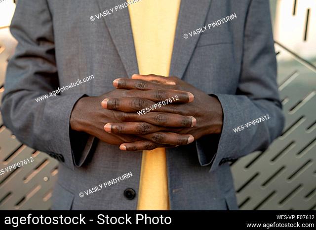 Businessman with hands clasped in front of metal wall