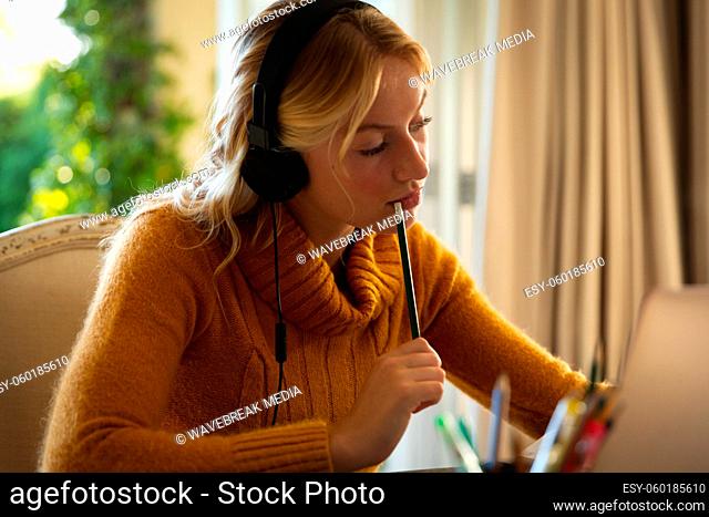 Caucasian woman working in living room at home, wearing headphones and using laptop, concentrating