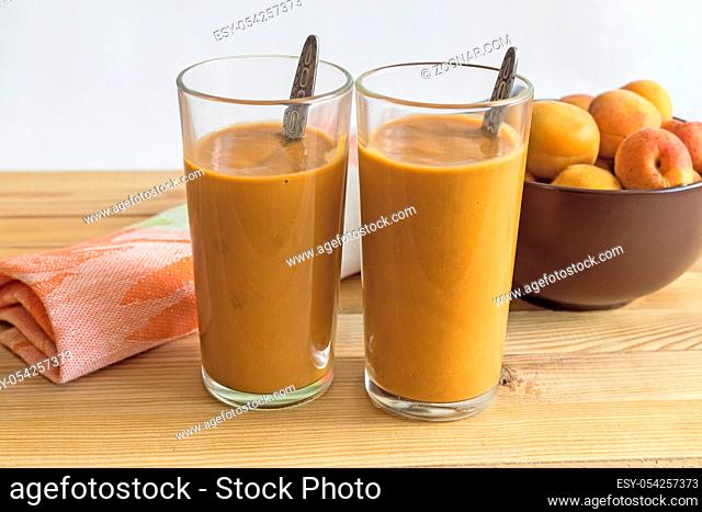 Two glass cups with apricot smoothie on the table on a napkin. Next to the apricots in a glass vase