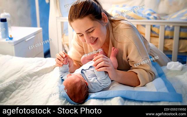 Portrait of beautiful mother holding hands of her little baby son lying on bed at night