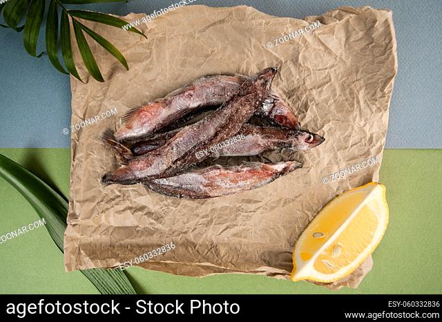 The raw frozen capelin rests on the kraft paper on a light blue-green background