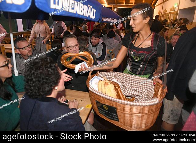 22 September 2023, Bavaria, Munich: The saleswoman Hiba Kalaai stops with her basket of bread goods at a table in the Schützenzelt and sells a pretzel