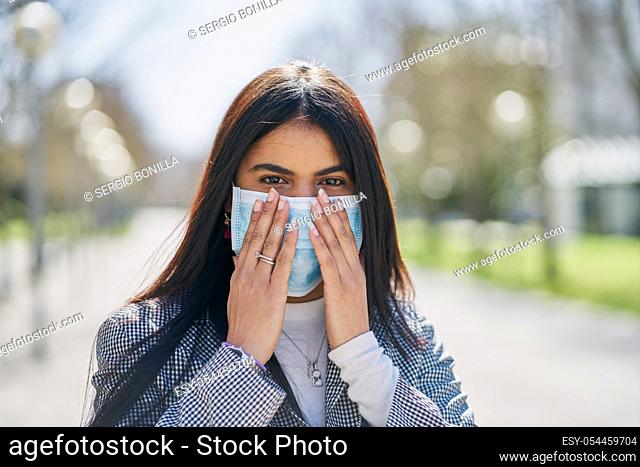 Girl putting on a protective mask to avoid contagion while walking down the street. Coronavirus concept