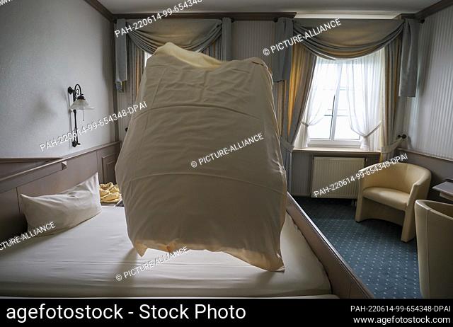 08 June 2022, Saxony, Hohenstein-Ernstthal: An employee of the Hotel Drei Schwanen shakes up a bedspread in a hotel room
