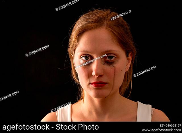 Blonde female with sad expression from front on black background. Young woman crying with blank look in darkenss. Upset female without smile in depression