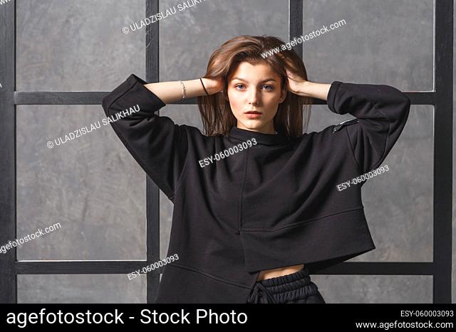 Young woman in black sportswear, pants and sweatshirt. Concept of fashionable sport outfit, indoors photo. Copy space