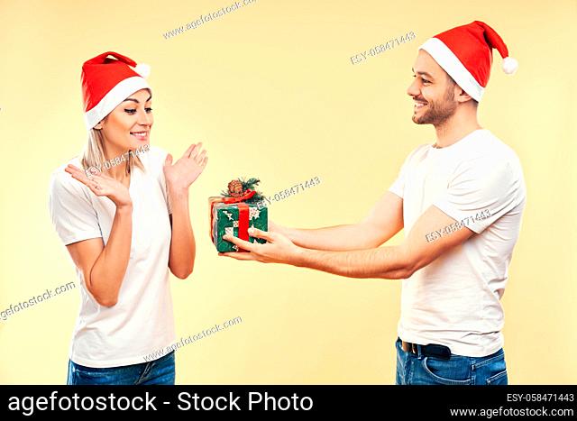 Young man give Christmas gift box to woman isolated on beige background. Present, holiday, celebration concept