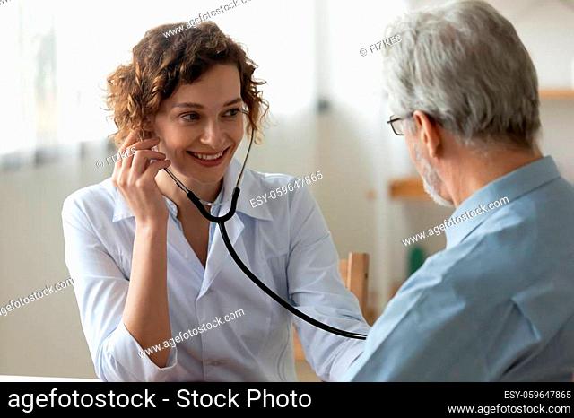 Smiling young female nurse listen to heart rate do regular checkup of mature male patient, positive woman doctor use stethoscope phonendoscope examine senior...