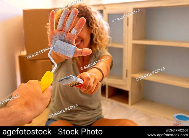 Mature man painting female friends hand with paint roller at home
