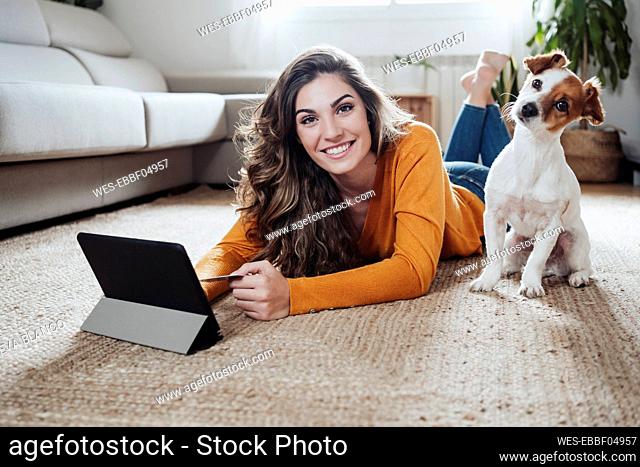 Woman with tablet PC lying on floor with dog at home