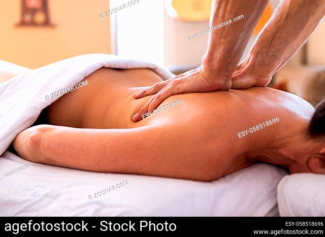 A young woman getting relaxing back massage in the spa salon. Medium shot of masseur hands giving massage therapy. Female enjoying a massage