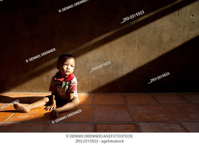 A toddler sits in a shaft of light in a village outside of Phnom Penh, Cambodia