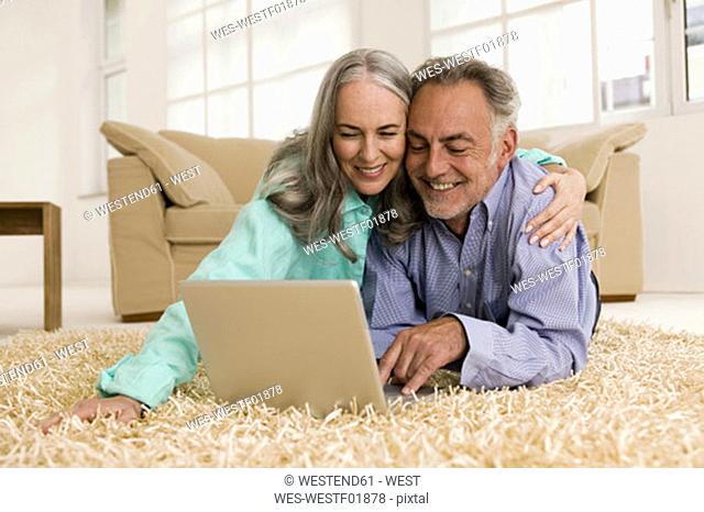 Mature couple lying on carpet, using laptop, smiling