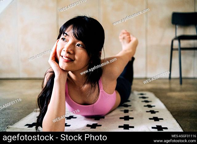 Young woman with hand on chin practicing yoga while day dreaming at home