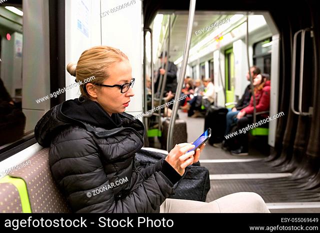 Cheerful young girl texting on mobile phone social network applications while traveling on metro. Wireless internet on public transport concept