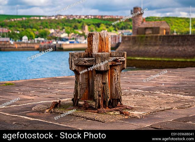 An old wooden ship bollard on the West Pier with the Marina in the background, seen in Whitehaven, Cumbria, England, UK