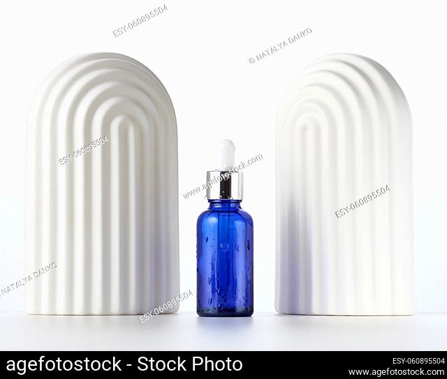 blue glass bottle with a pipette and white decorative arches on a white background. Template for cosmetic liquid products, advertising and promotion