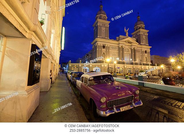 View to the Nuestra Senora de la Asuncion Cathedral by night with a Vintage American car in the foreground at Parque Cespedes, Santiago de Cuba, Cuba