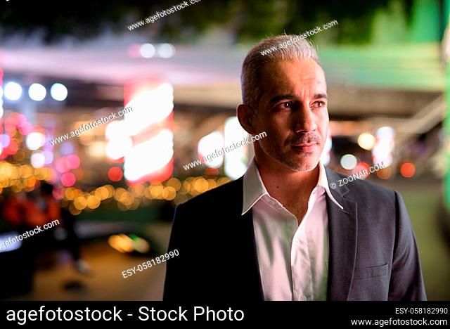 Handsome Persian businessman wearing suit in city at night
