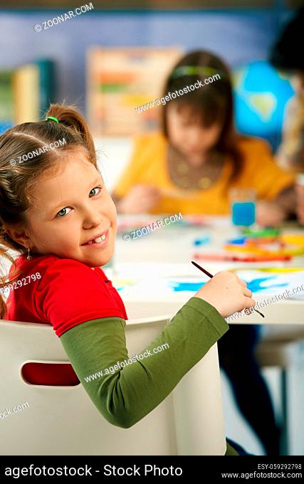 Portrait of happy elementary age child sitting at desk looking at camera in art class in primary school classroom, smiling